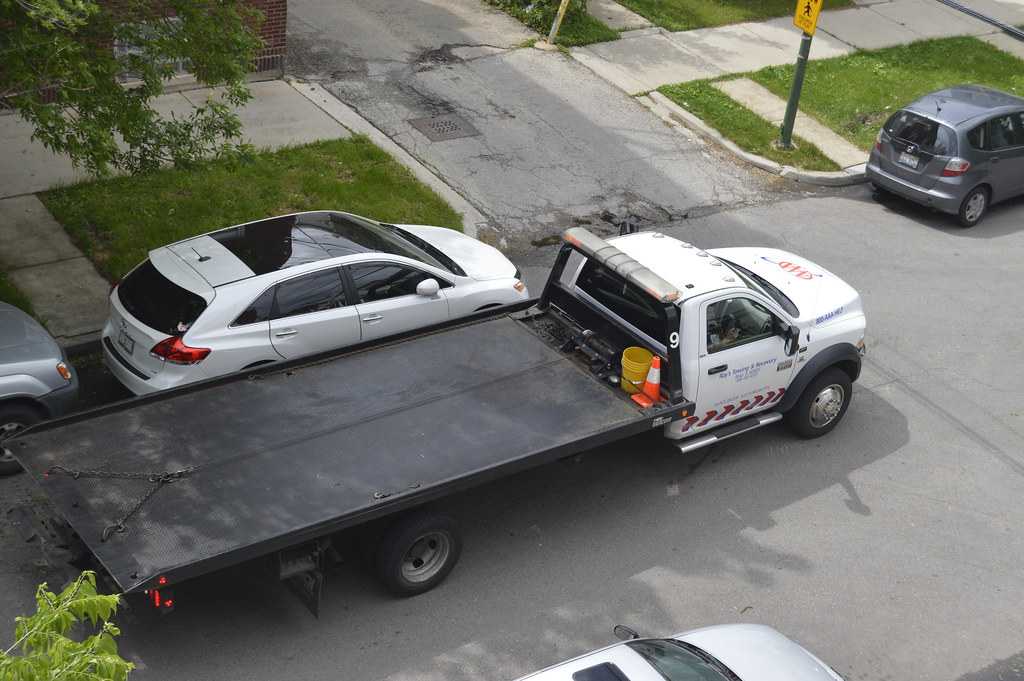 White rollback tow truck with red and blue striping, flatbed ready to haul a junk car in a Monroe NC neighborhood